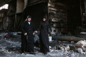 Women walk past damaged shop as they flee towards safer parts of Manbij city, in Aleppo Governorate, Syria, August 10, 2016. REUTERS/Rodi Said